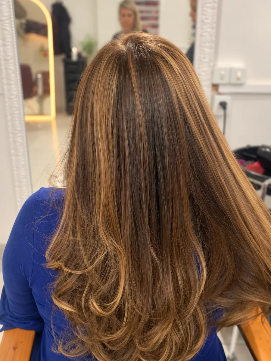 A mesma cliente antes e depois: do castanho com frizz ao castanho iluminado com mechas caramelo, liso e alinhado